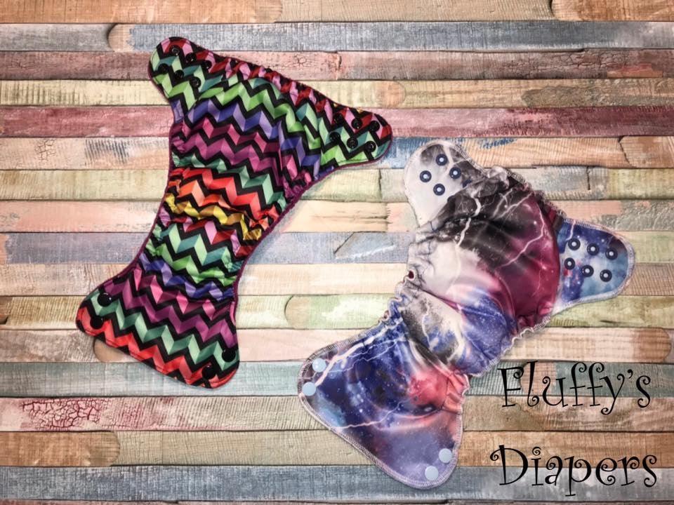 Two Fluffy's Diapers reusable cloth diapers with rainbow chevron and galaxy prints on wood.