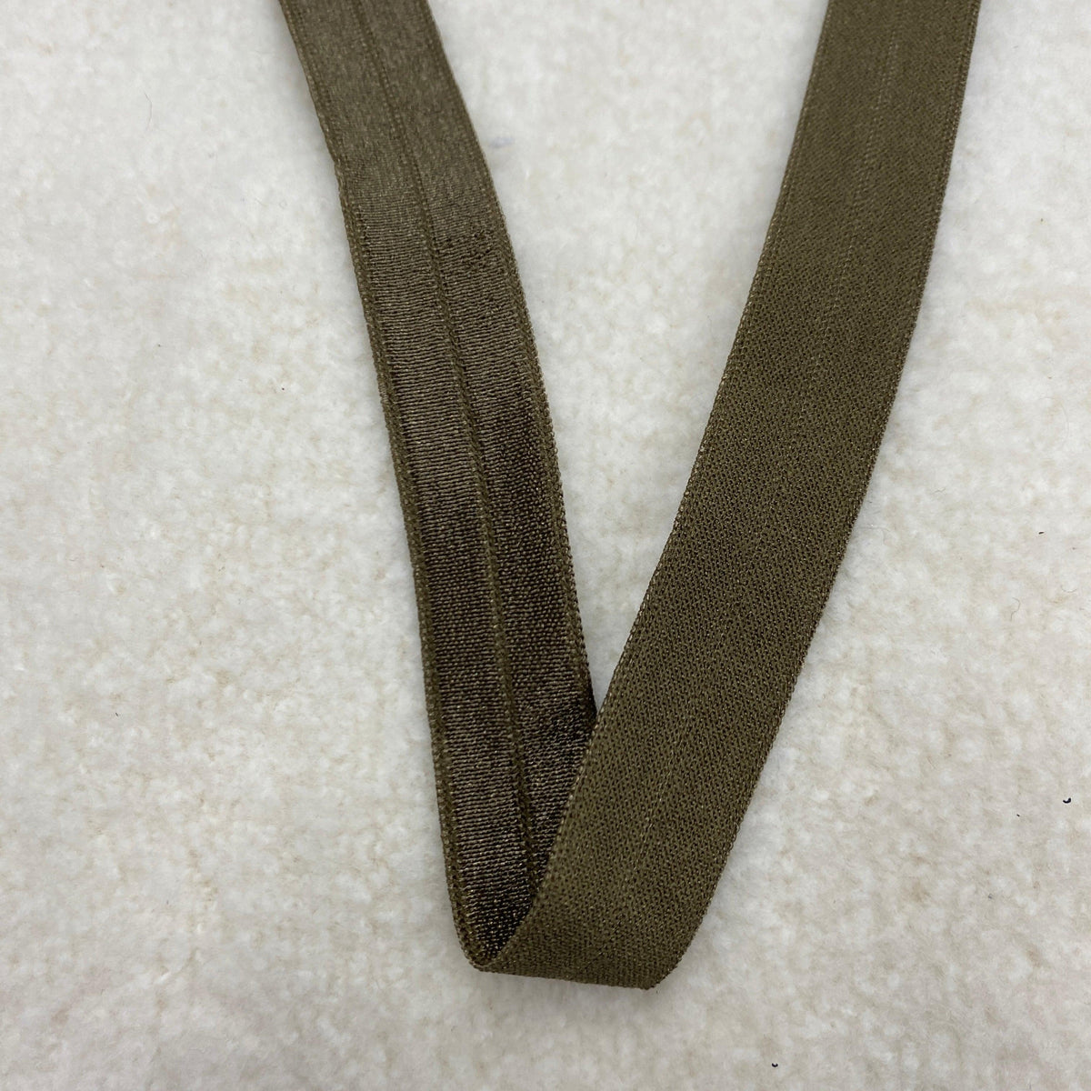 Olive green elastic band from Nature's Fabrics on a white textured surface.