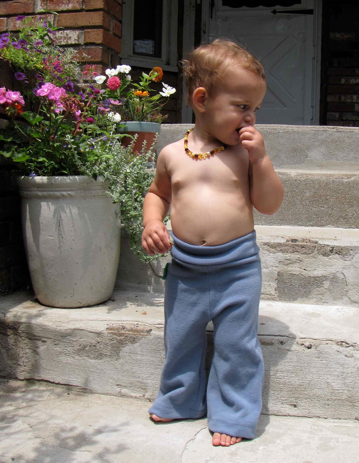 A toddler wearing Nature's Fabrics blue natural fiber pants and a flower necklace.