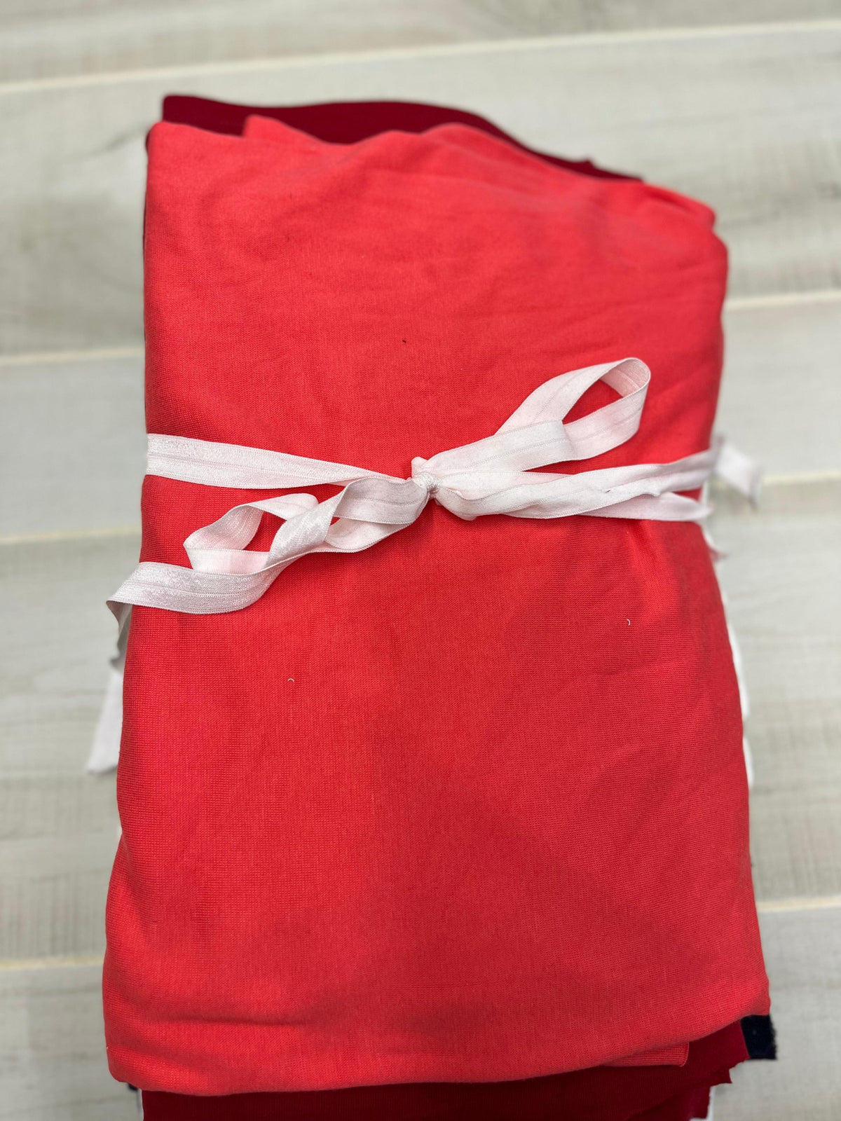 A folded bolt of red organic cotton fabric from Nature's Fabrics tied with a white ribbon.