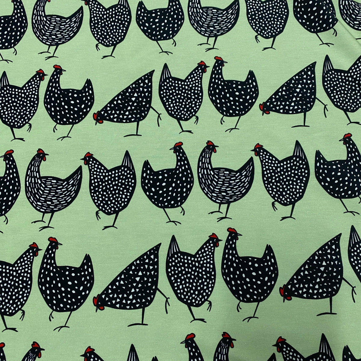 Nature's Fabrics light green cotton fabric featuring a pattern of black speckled chickens.