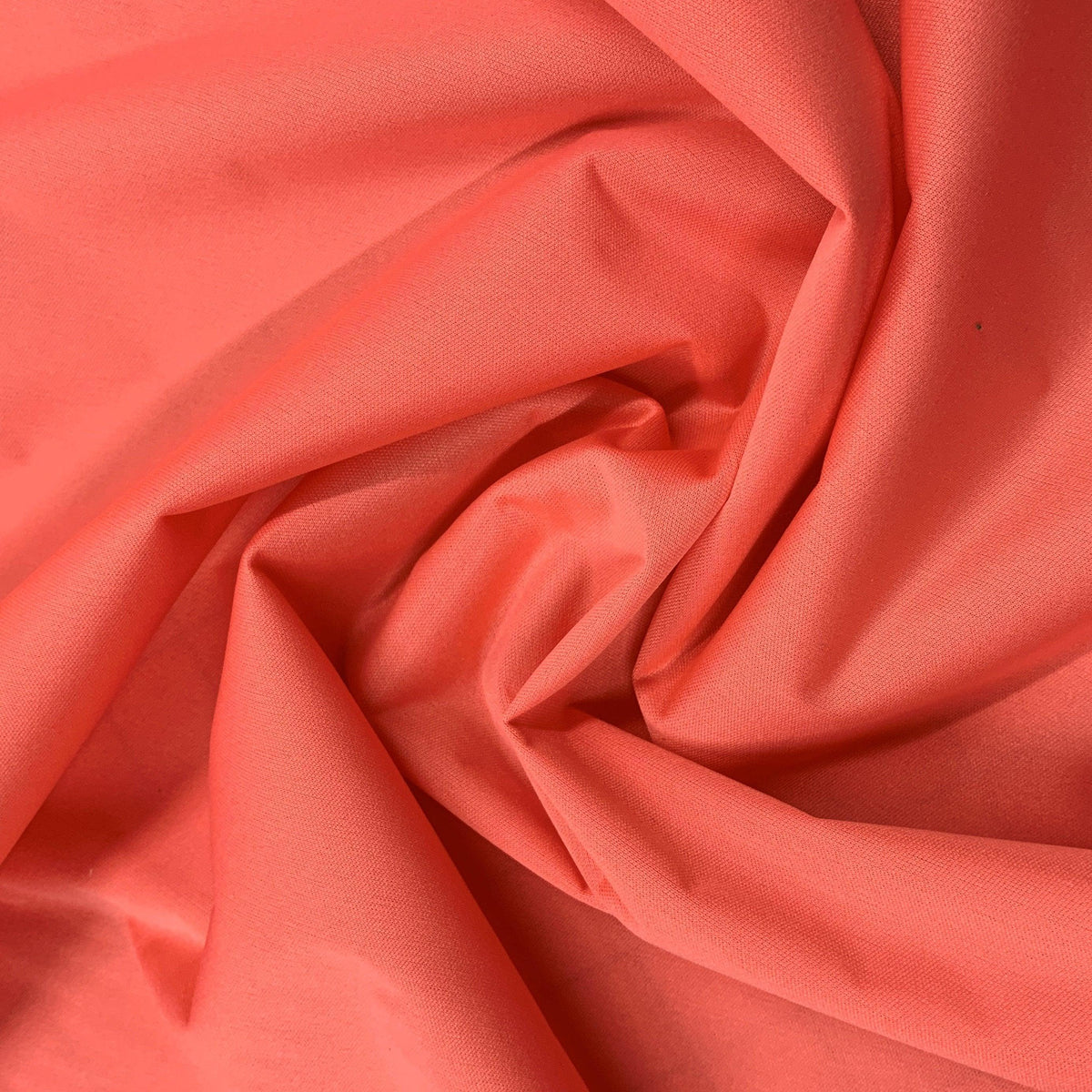 Nature's Fabrics coral red organic cotton fabric with elegant folds and swirls.
