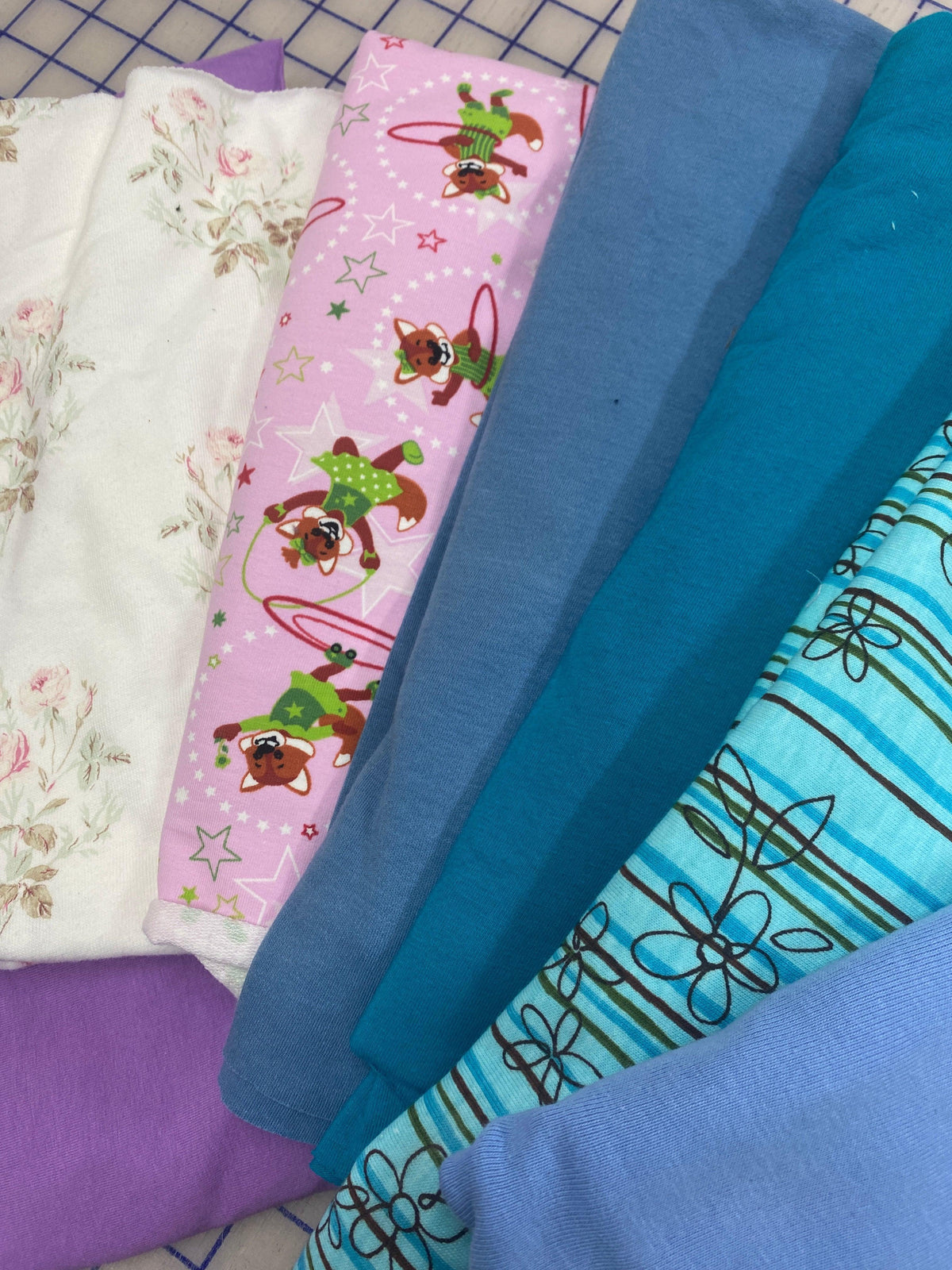 Assorted Nature's Fabrics textile bolts in white floral, pink patterned, and blue tones.
