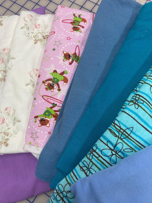 Assorted Nature's Fabrics textile bolts in white floral, pink patterned, and blue tones.