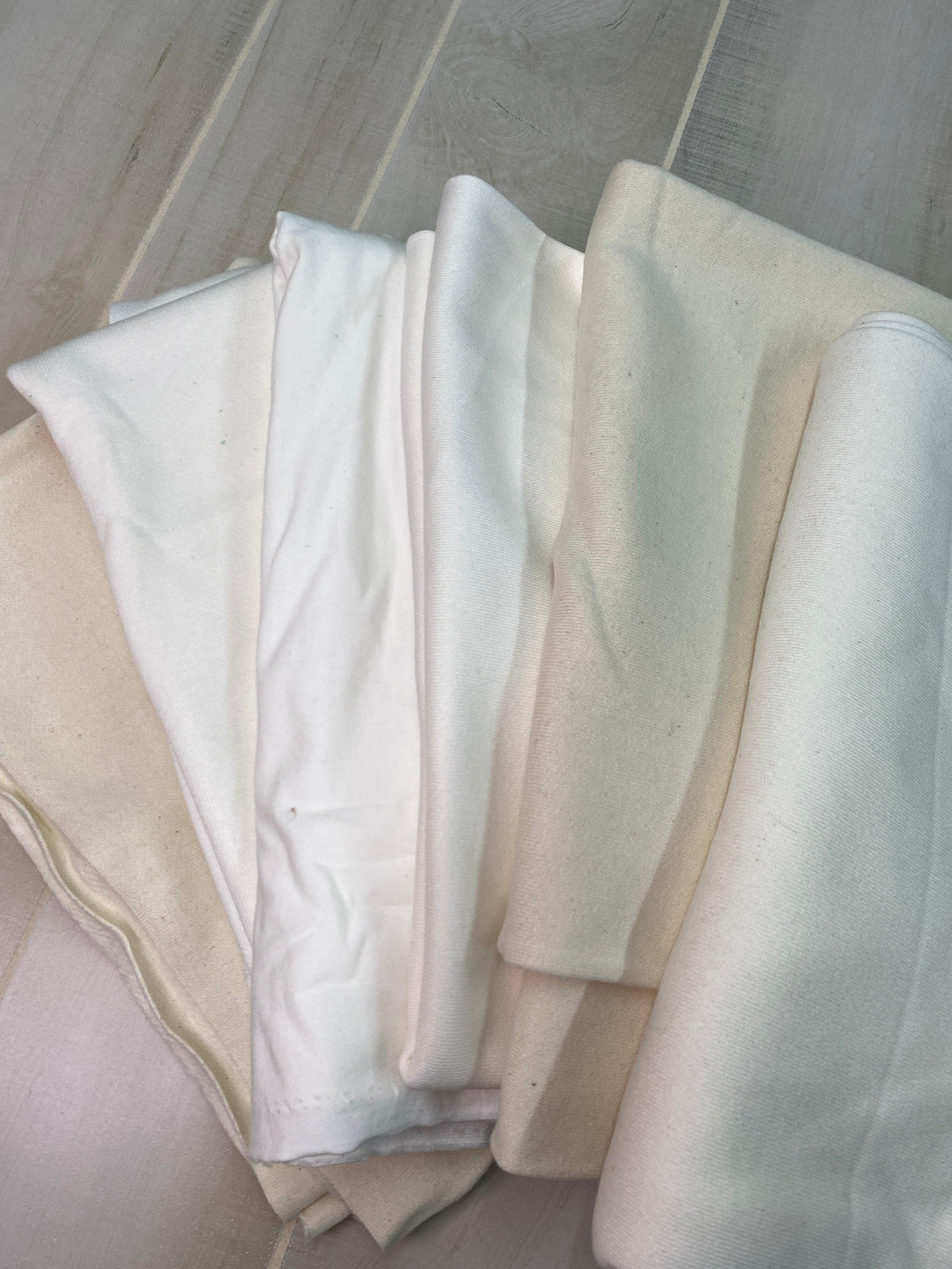 Folded premium natural white fabric bolts from Nature's Fabrics on a light wood surface.