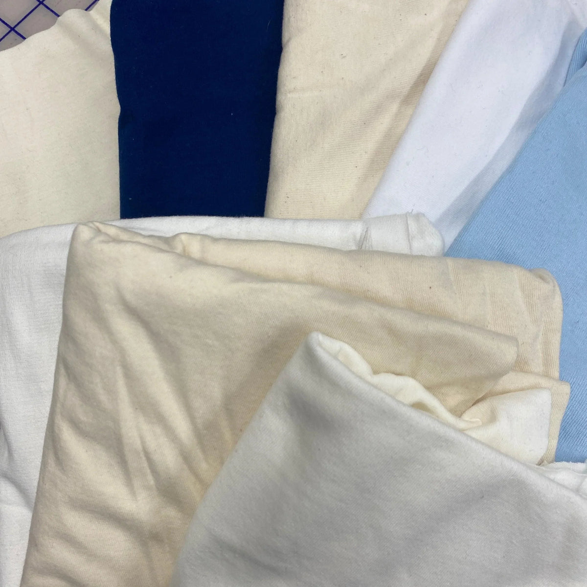 Nature's Fabrics collection of folded organic cotton fabrics in navy, cream, white, and light blue.