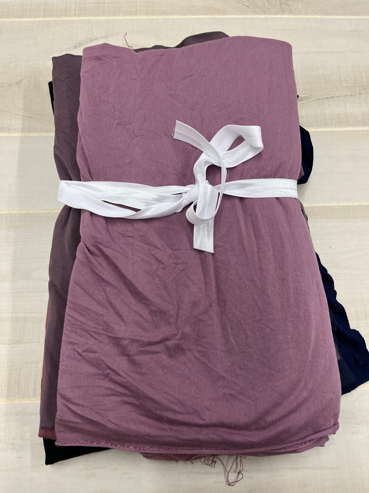 Stacked folds of mauve and dark purple Nature's Fabrics tied with a white ribbon.