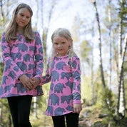 Two girls wearing pink elephant print dresses by Nature's Fabrics in a forest setting.