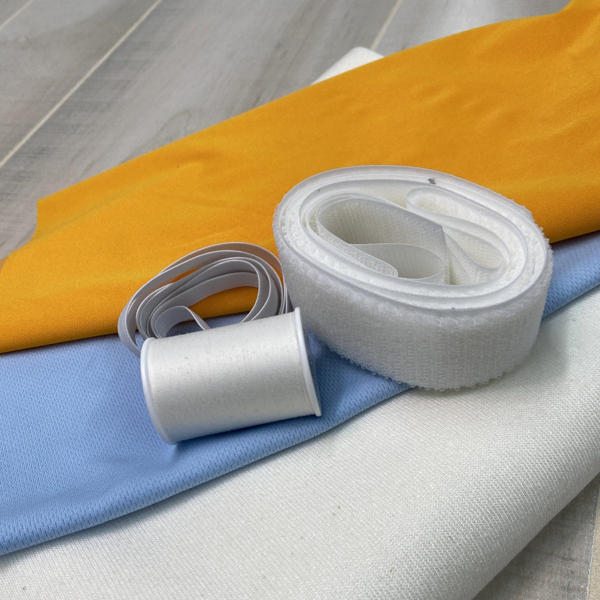 Nature's Fabrics white adhesive strap and rolls over yellow and blue fabric swatches