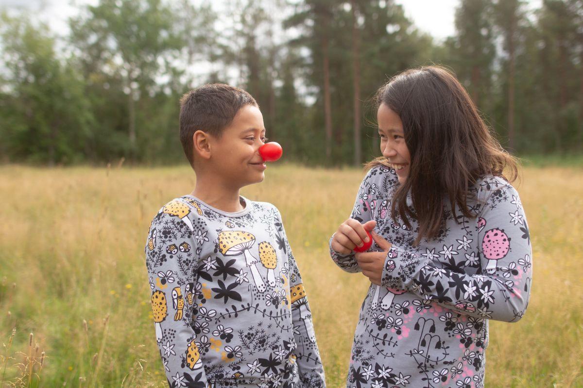 Two children wearing Nature's Fabrics mushroom print pajamas playing in a grassy field.