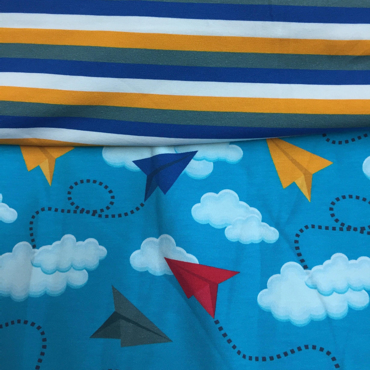 Nature's Fabrics blue fabric with paper planes and clouds next to striped fabric