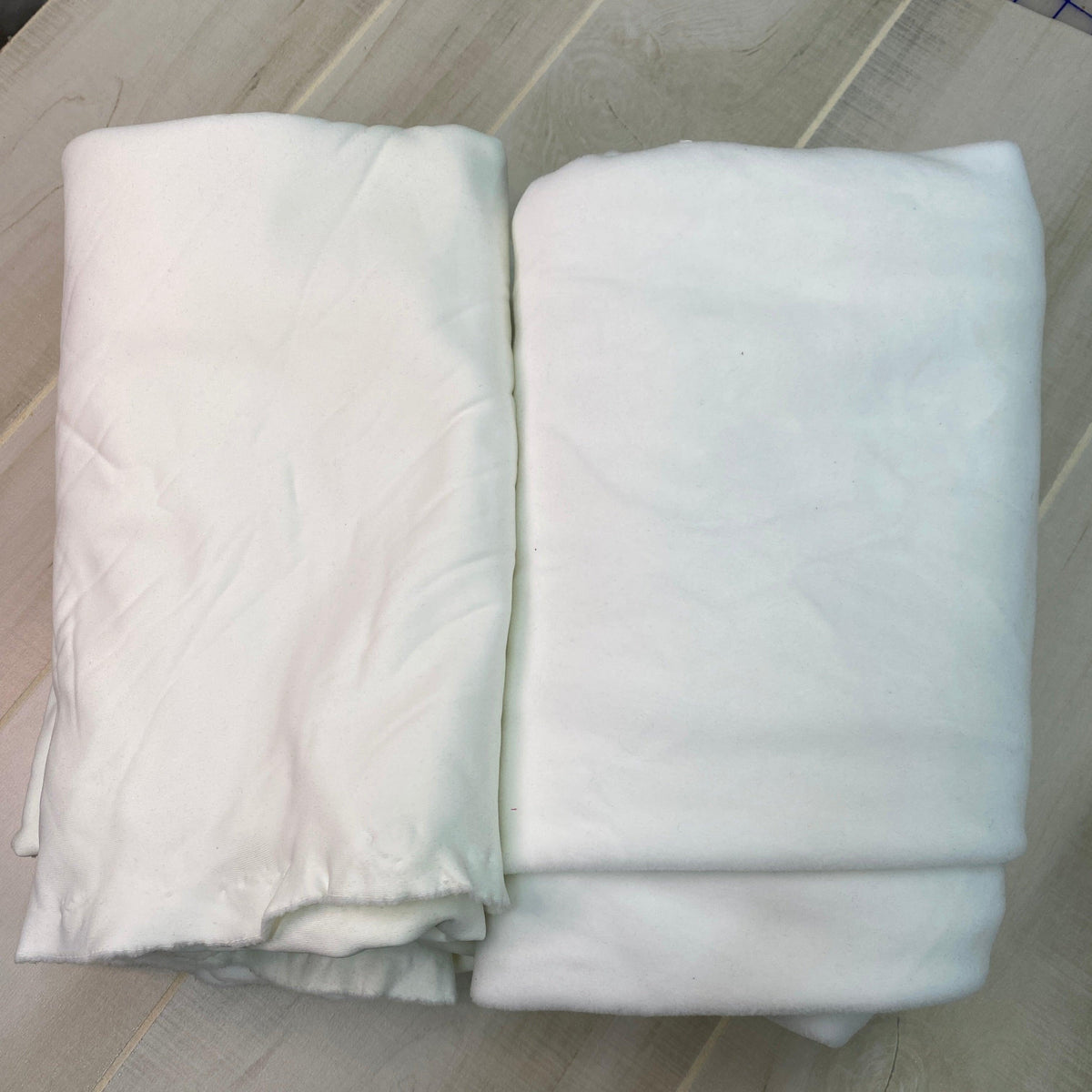 Two folded pieces of white premium natural fabric from Nature's Fabrics on a light wood surface.
