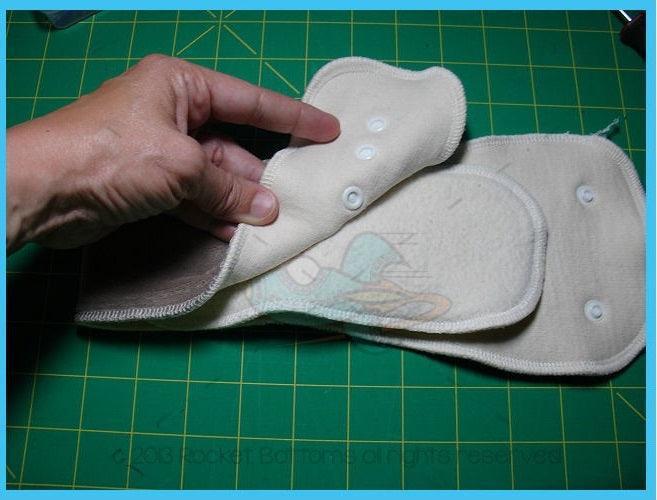 Hand holding Nature's Fabrics reusable cloth diaper inserts on a green cutting mat