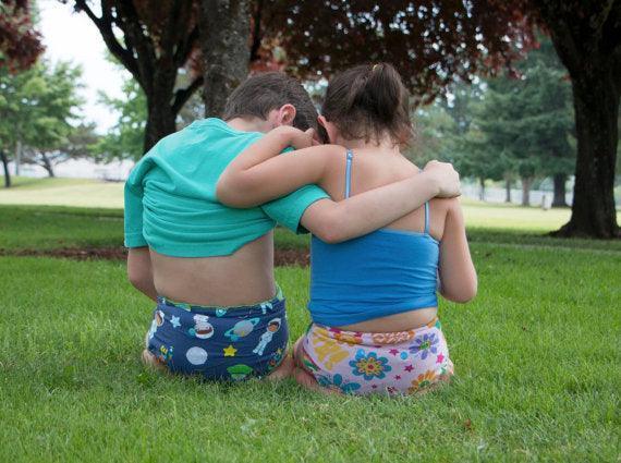 Two children hugging in a grassy park wearing Nature's Fabrics patterned underwear.