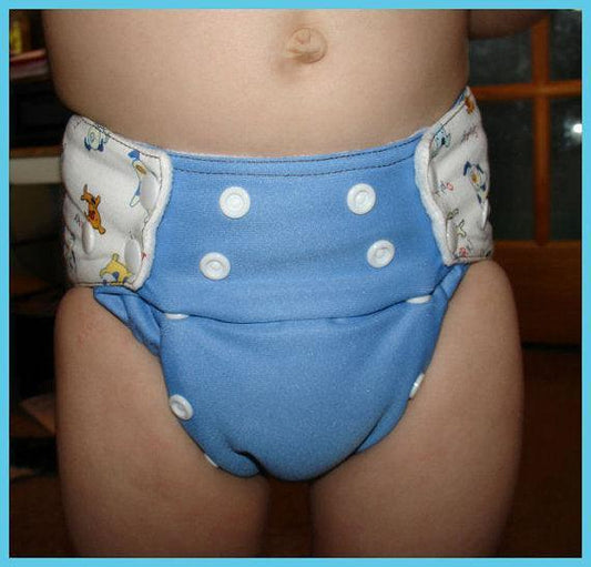 A baby wearing a blue Nature's Fabrics reusable cloth diaper with snap closures.