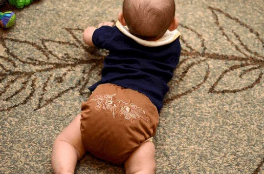 Baby wearing a Nature's Fabrics brown patterned cloth diaper and navy blue shirt on a rug.
