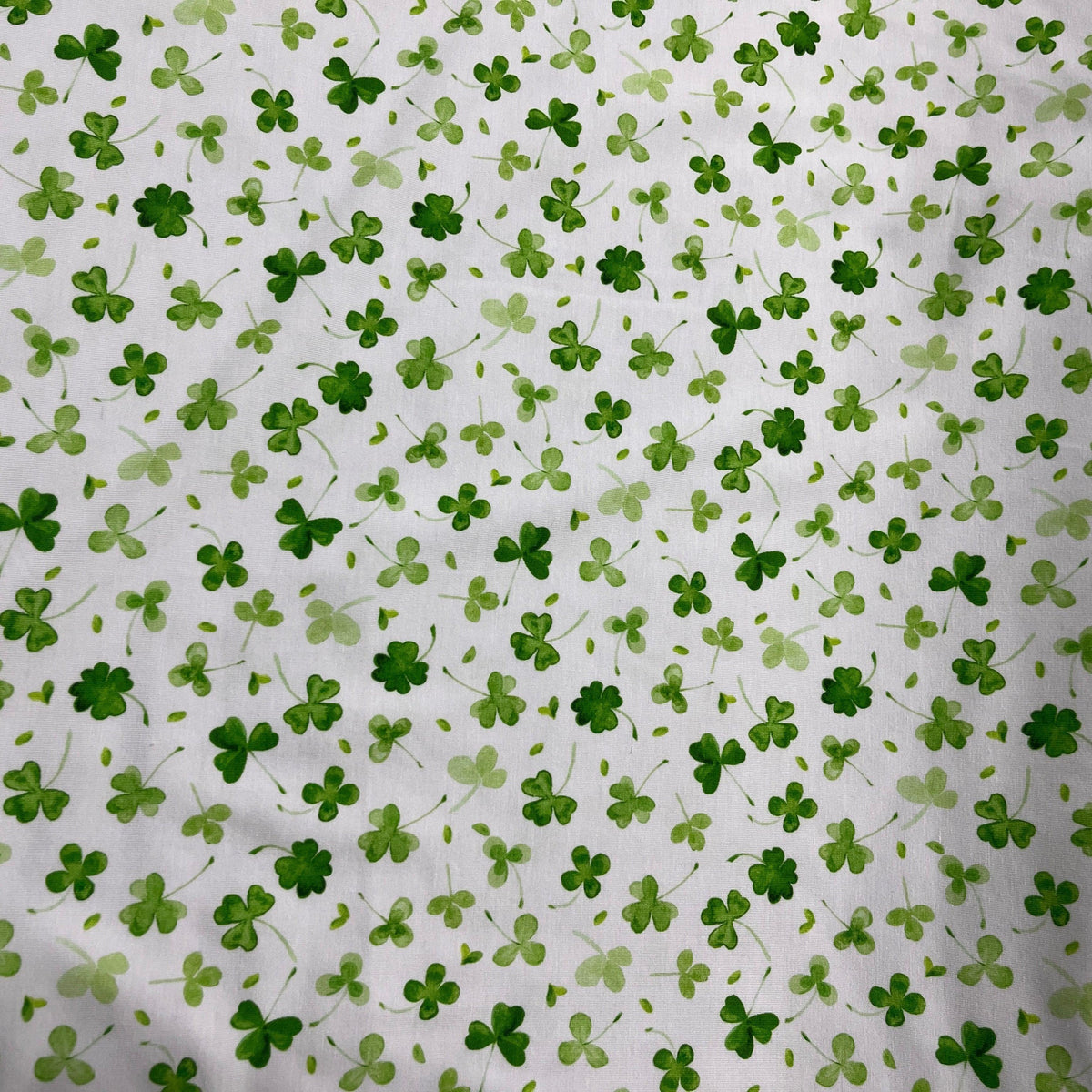 Nature's Fabrics white fabric with a pattern of green clovers.