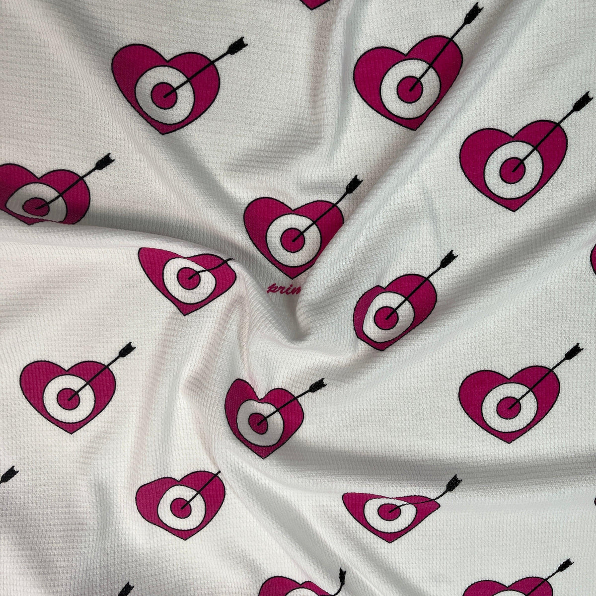 Nature's Fabrics white textured fabric with pink heart target and arrow pattern