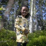 A child wearing a Nature's Fabrics yellow patterned long-sleeve shirt in a forest.