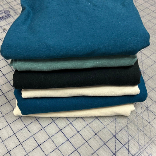 Stack of assorted solid hemp stretch jersey fabric in blue, black, and cream shades on a grid cutting mat.