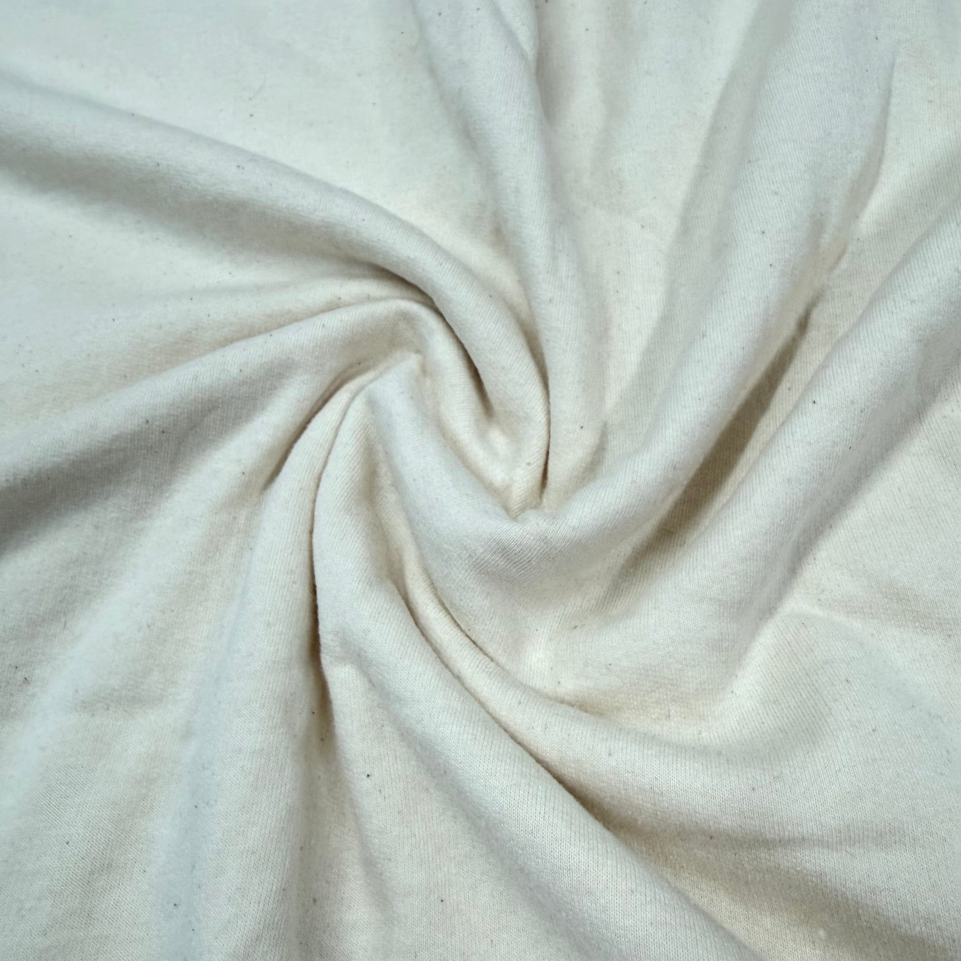 Natural off-white cotton fabric swirled in soft folds, showcasing texture — Nature's Fabrics