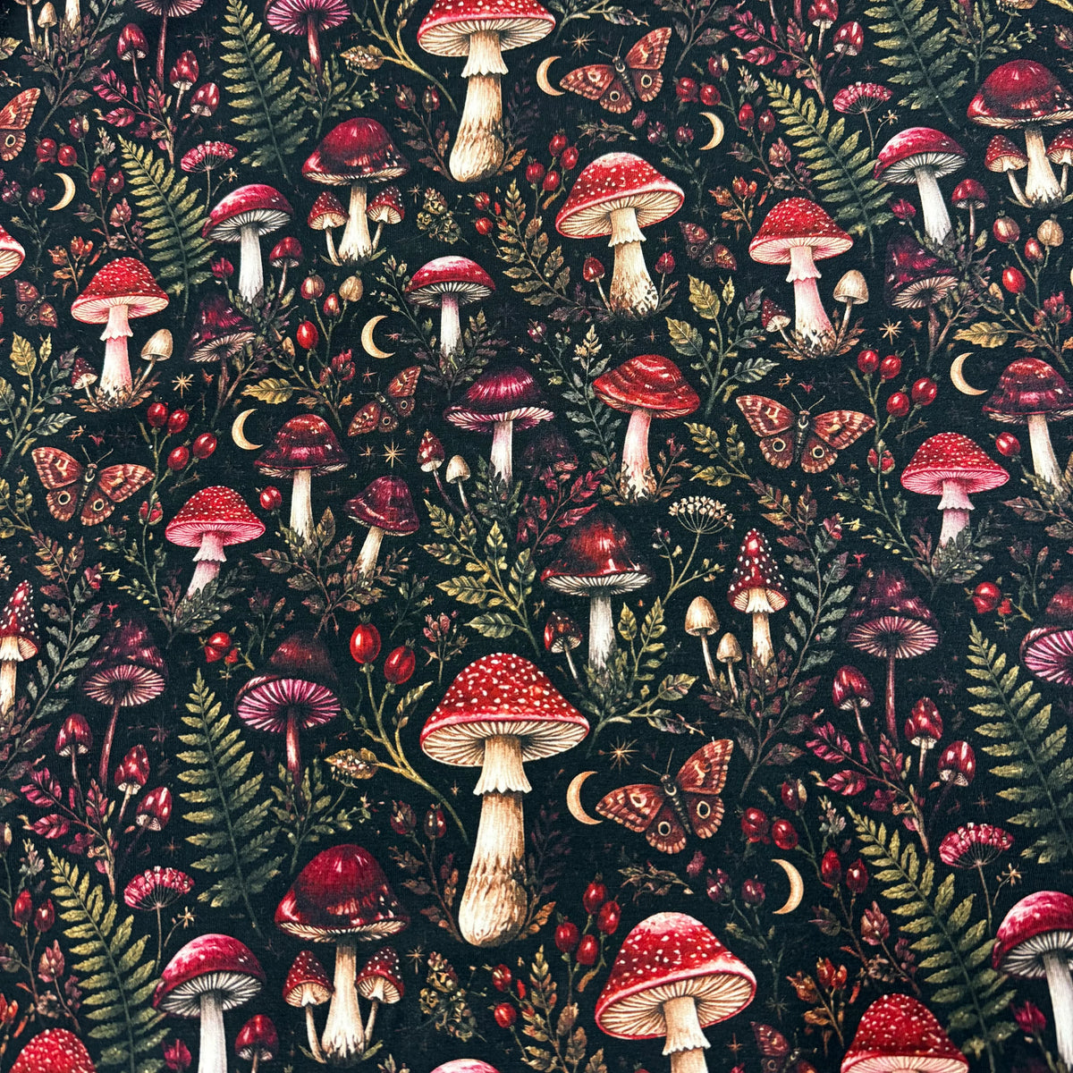Nature's Fabrics dark forest print fabric with red mushrooms, ferns, and moons.